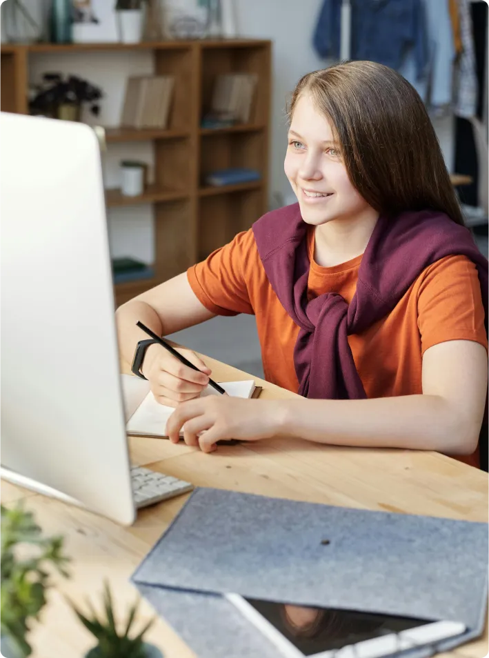 A girl studying on her computer while taking notes on a book